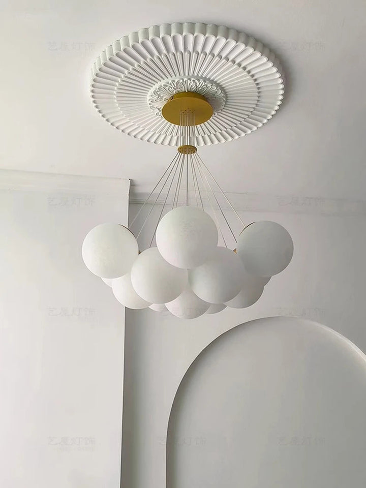 Suspension design à globes en verre opalin blanc installée sous un plafond à moulures décoratives avec rosace en laiton.