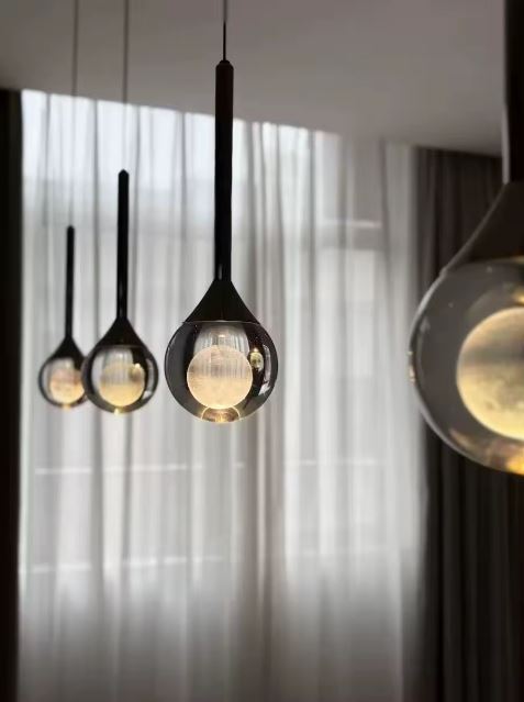 Alignement de suspensions goutte en verre et métal noir, luminaire design contemporain jouant sur la transparence.