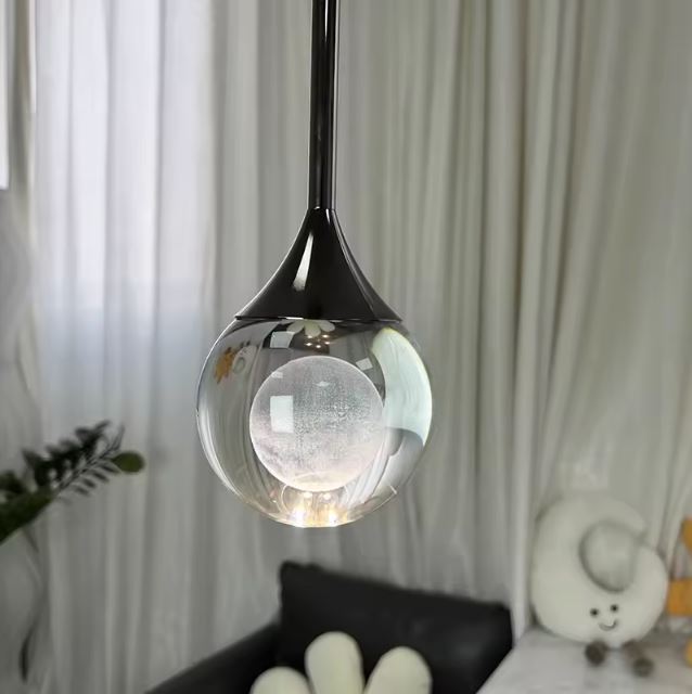 Suspension goutte en verre transparent et métal noir diffusant une lumière douce, luminaire design contemporain et raffiné.