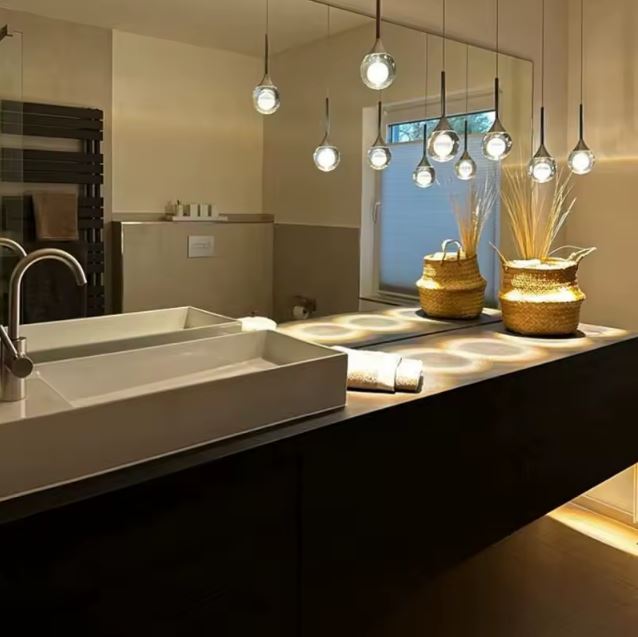 Suspension goutte en verre cristallin et métal noir au-dessus d’un îlot vasque, éclairage design contemporain pour salle de bain.