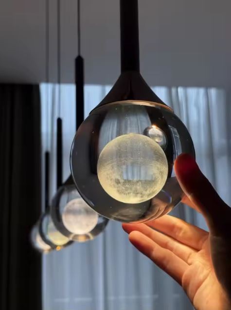 Suspension goutte en verre transparent avec sphère lumineuse givrée, effet bijou suspendu au style contemporain.