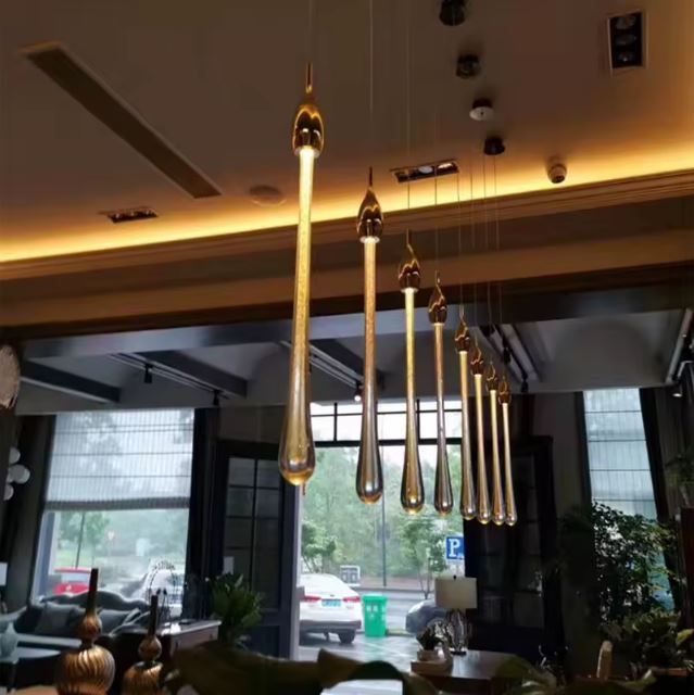 Suspension en gouttes dorées allongées, parfaite au-dessus d’une table de salle à manger moderne ou d’un comptoir élégant et lumineux.
