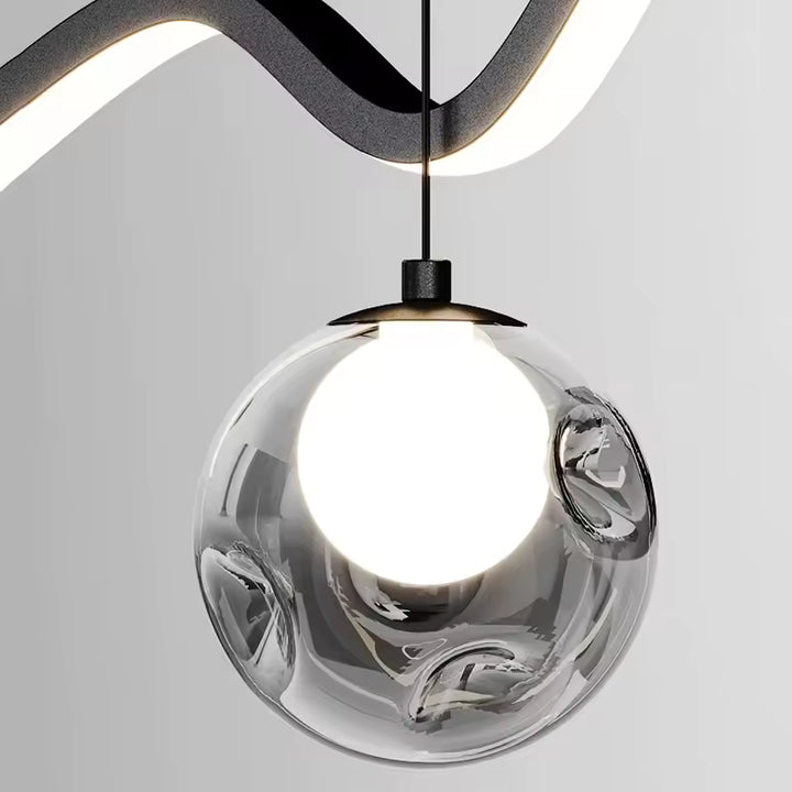 Gros plan sur un globe en verre transparent suspendu sous une ligne LED ondulée, au design sculptural et contemporain.