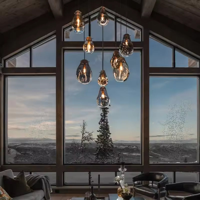 Devant une grande baie vitrée, un lustre en cascade à huit globes de verre soufflé fumé illumine un salon au style chalet chic.
