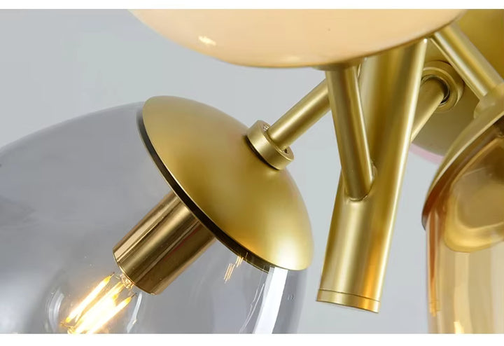 Gros plan sur la structure dorée d’une suspension rétro en verre coloré avec globe fumé et finitions raffinées
