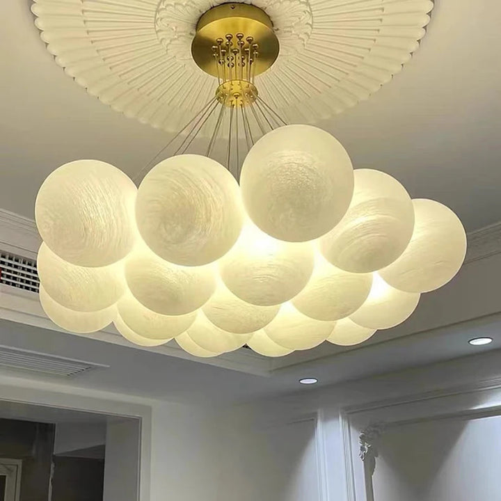 Gros plan d'une suspension design à 19 globes en verre opalin blanc avec rosace dorée et éclairage chaleureux