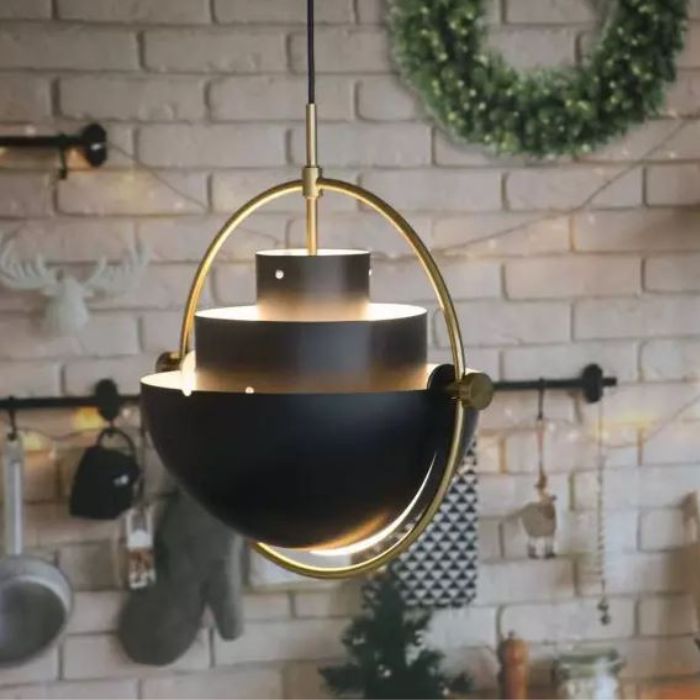 Suspension Gubi Multi Lite noire avec cadre doré, éclairant un intérieur cosy au style rustique avec un mur en briques.