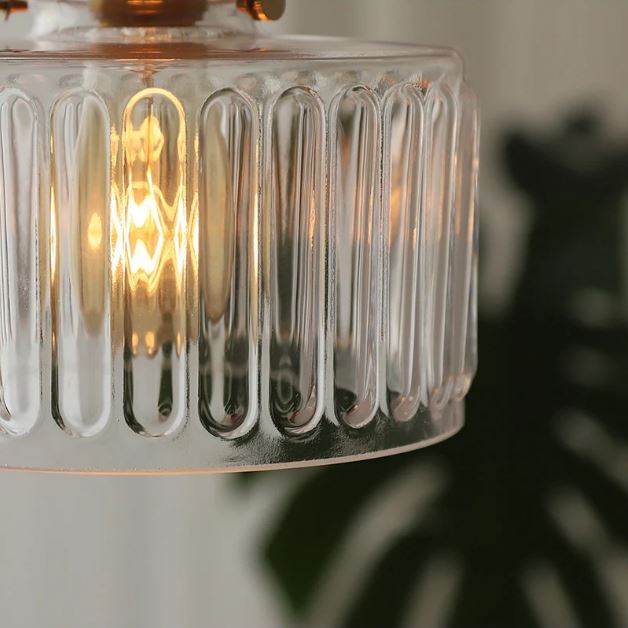 Gros plan sur une suspension holophane en verre strié avec lumière chaude, idéale pour une ambiance feutrée et élégante.