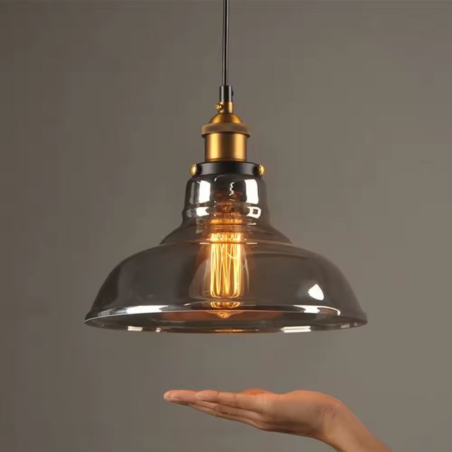 Suspension industrielle en verre avec ampoule Edison, mise en valeur par une main pour illustrer la taille et le design.