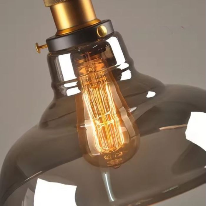 Détail de l'ampoule Edison et de l'abat-jour en verre d'une suspension industrielle, offrant un éclairage chaleureux.