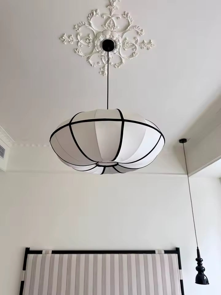 Vue de dessous d'une suspension japonaise sculpturale aux pétales blancs soulignés de noir, sous un plafond ornementé.