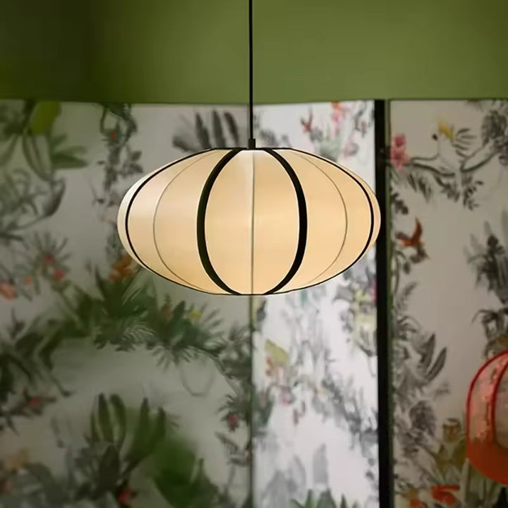 Lanterne suspendue japonaise aux courbes arrondies et lignes noires, diffusant une lumière chaleureuse dans un décor végétal.