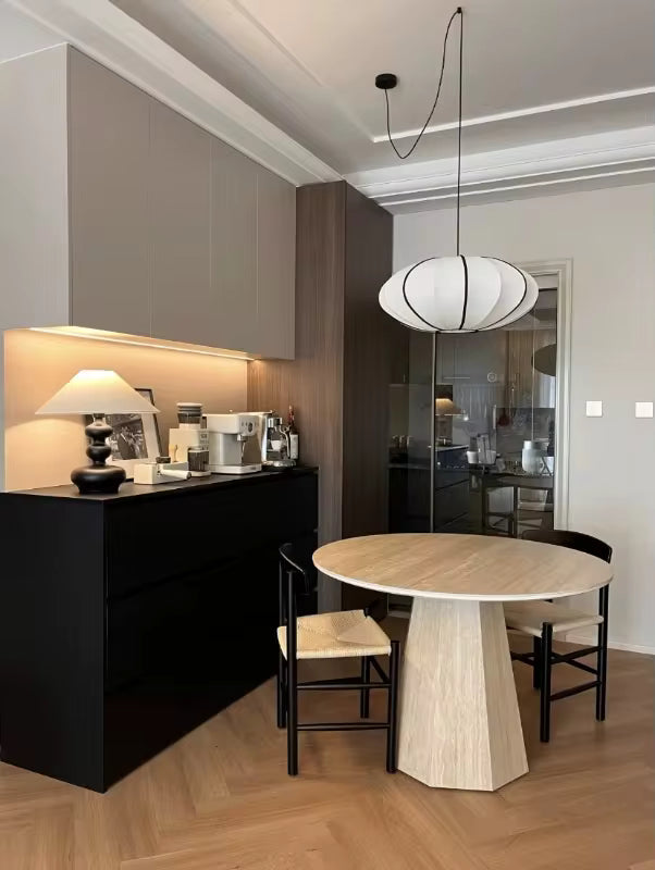 Au-dessus d'une table ronde en bois, suspension japonaise blanche aux lignes noires, dans une salle à manger contemporaine.