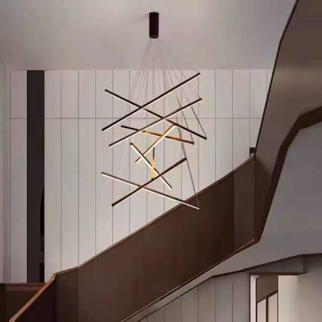 Suspension LED en tiges lumineuses croisées, suspendue au-dessus d’un escalier contemporain dans un intérieur au style graphique moderne.