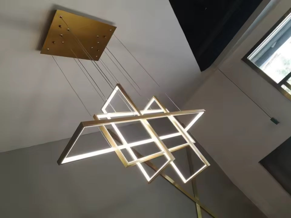 Suspension LED dorée aux cadres lumineux croisés, vue en contre-plongée révélant son architecture graphique et contemporaine.