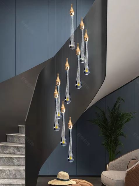 Suspension LED en forme de gouttes dorées éclairant une montée d’escalier moderne avec mur bleu nuit et coin salon cosy.