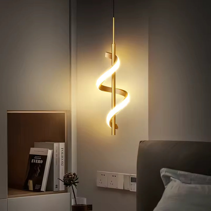Près d'un lit, suspension LED dorée en spirale hélicoïdale diffusant une lumière chaude, au design sculptural et moderne.
