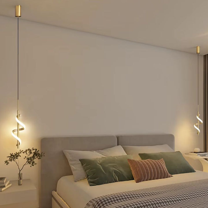 De chaque côté d'un lit, deux suspensions LED dorées en spirale lumineuse créent une ambiance douce et contemporaine.
