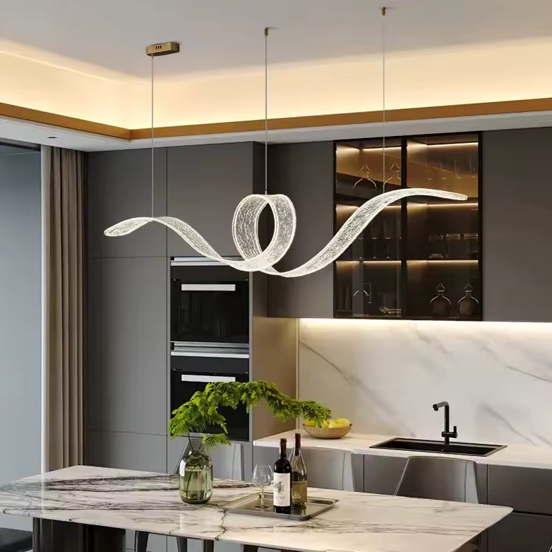 Une suspension LED sculpturale en ruban lumineux ondulé forme une boucle élégante au-dessus d'un îlot en marbre.