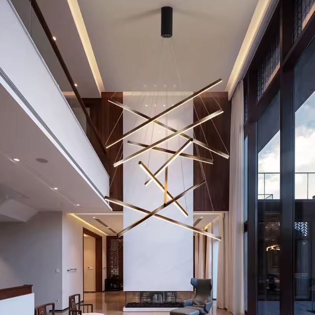 Suspension contemporaine en tiges LED croisées suspendue dans un salon lumineux à double hauteur sous plafond avec grandes baies vitrées.