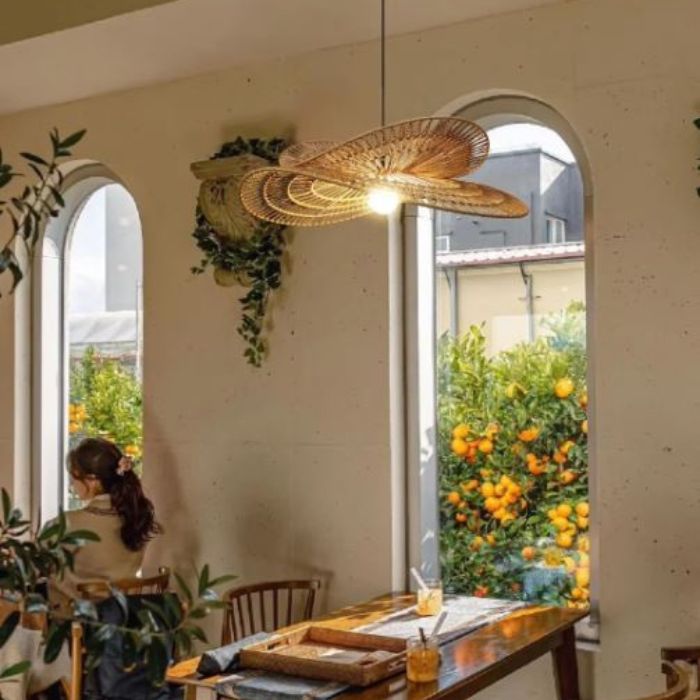 Suspension libellule en rotin suspendue au-dessus d'une table en bois, offrant une vue apaisante sur un jardin d'orangers.
