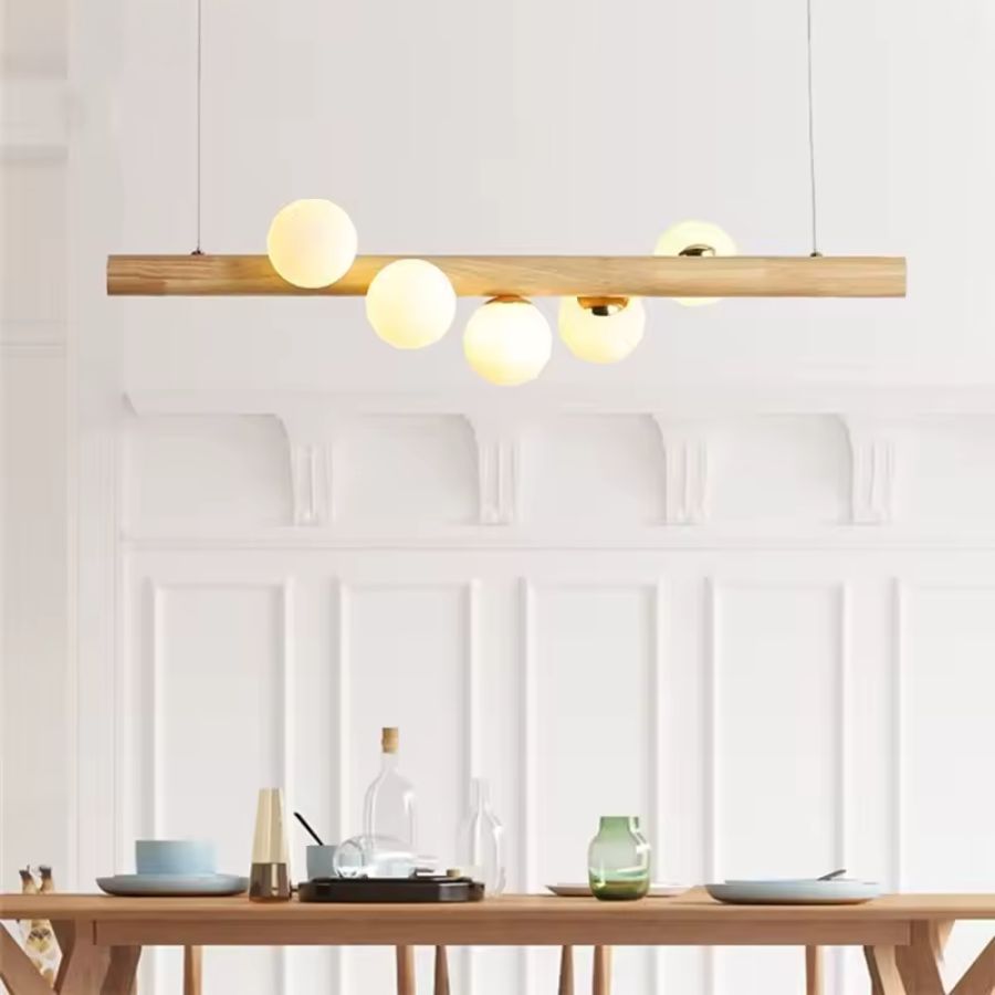 Suspension linéaire en bois clair et globes lumineux au-dessus d’une table, dans un esprit minimaliste et nordique.