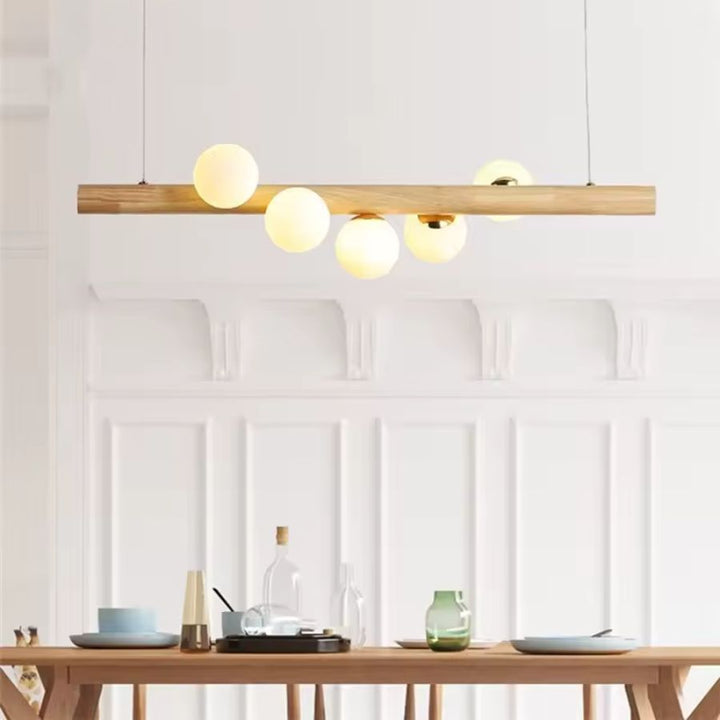 Suspension linéaire en bois clair et globes lumineux au-dessus d’une table, dans un esprit minimaliste et nordique.