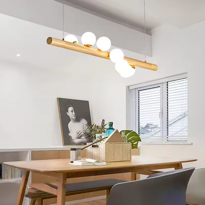 Dans cette salle à manger lumineuse, la suspension en bois clair et globes blancs affirme un style scandinave doux et épuré.