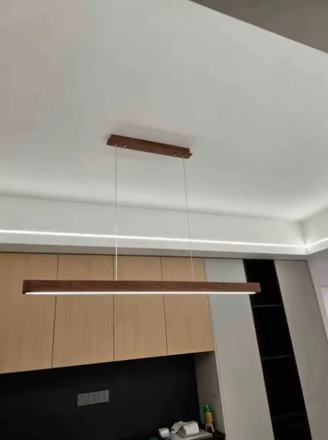 Suspension linéaire en bois foncé avec LED intégrée, luminaire minimaliste élégant idéal au-dessus d’une table à manger.