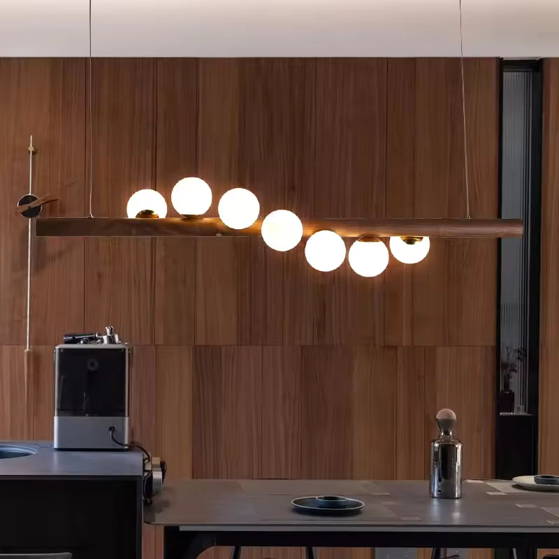 Dans une cuisine contemporaine, cette suspension linéaire en bois foncé à globes lumineux mêle esprit japandi et design chaleureux.