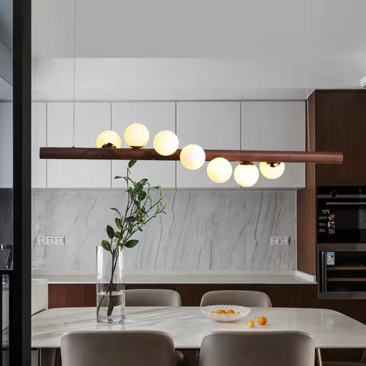 Lustre linéaire en bois foncé et globes lumineux dans une cuisine moderne, au style minimaliste et contemporain.