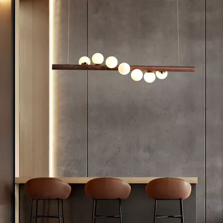 Au-dessus d’un îlot, cette suspension linéaire en bois à globes lumineux évoque un style japandi, moderne et épuré.