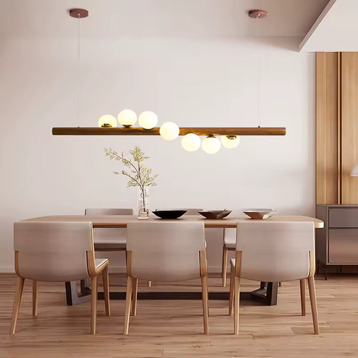 Au-dessus de la table, ce lustrelinéaire en bois et globes lumineux crée une ambiance japandi douce et chaleureuse.