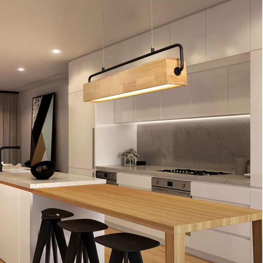 Dans une cuisine contemporaine, suspension linéaire en bois massif à armature noire, éclairant un îlot en bois clair.
