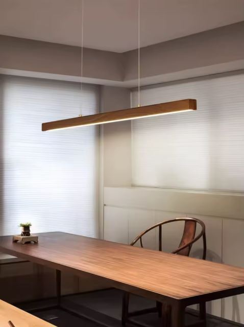 Suspension linéaire en bois naturel avec LED intégrée, luminaire japandi élégant au-dessus d’une table rectangulaire moderne.