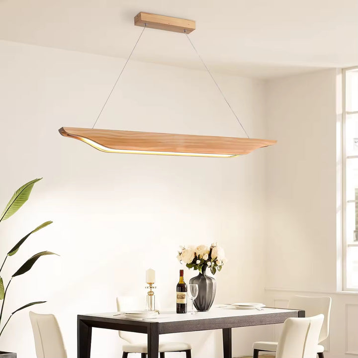 Suspendu au-dessus d'une table noire, ce luminaire en bois sculpté aux courbes fluides illumine une salle à manger contemporaine.