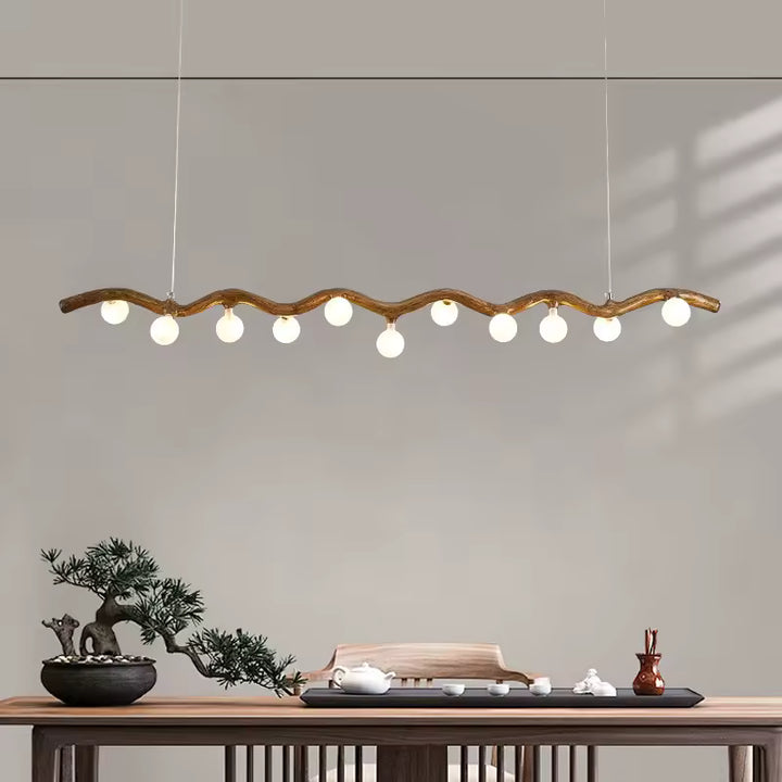 Suspension linéaire d'inspiration japandi, avec branche ondulée effet bois et globes blancs au-dessus d'un meuble en bois.