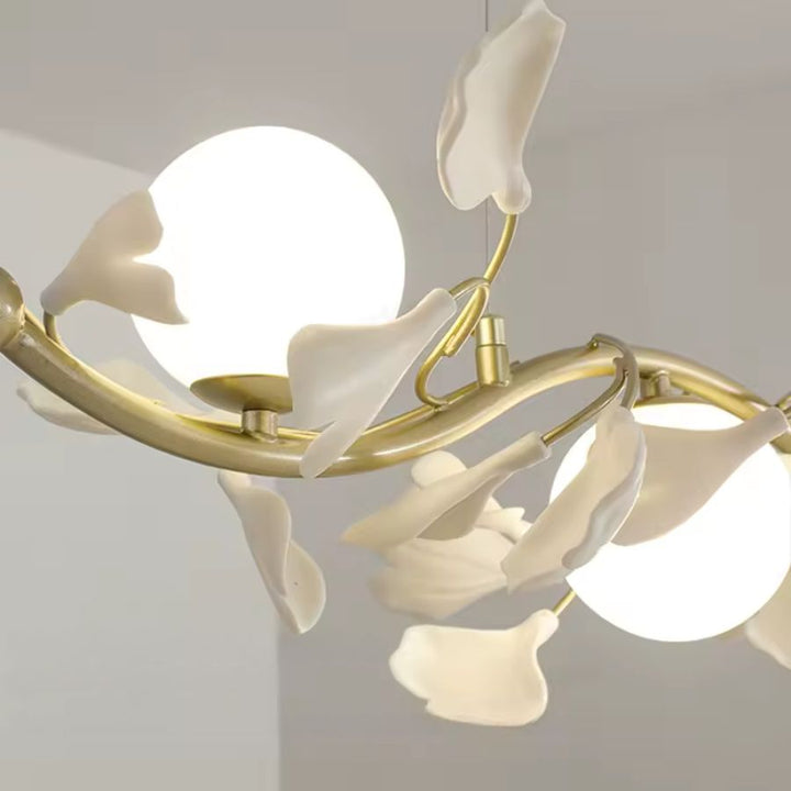 Détail des pétales blancs délicatement courbés autour des globes opalins d'une suspension florale dorée au design sculptural.