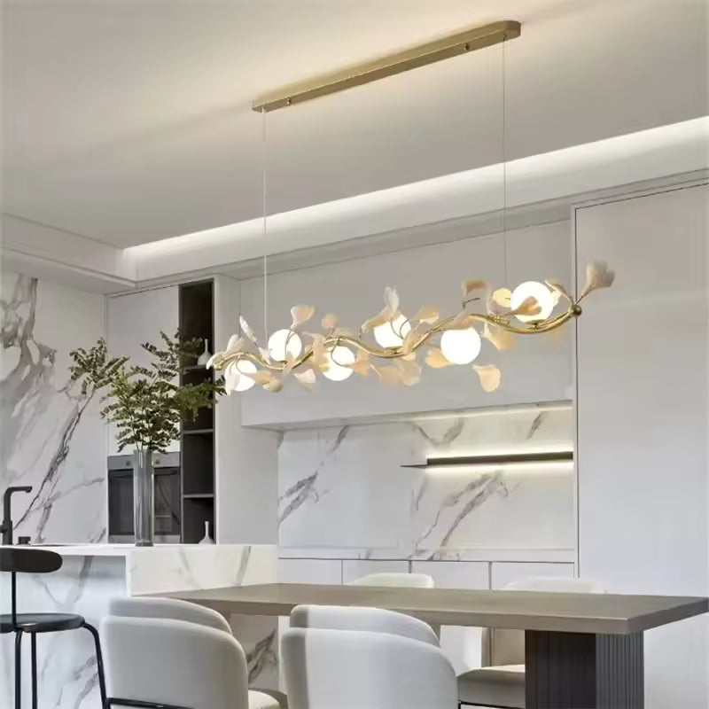 Dans une cuisine moderne en marbre, suspension florale à branches dorées et globes opalins, au design contemporain raffiné.