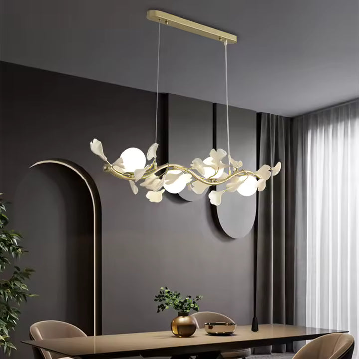 Au-dessus d'une table épurée, suspension florale à tiges dorées ondulantes et globes opalins, dans une salle à manger chic.
