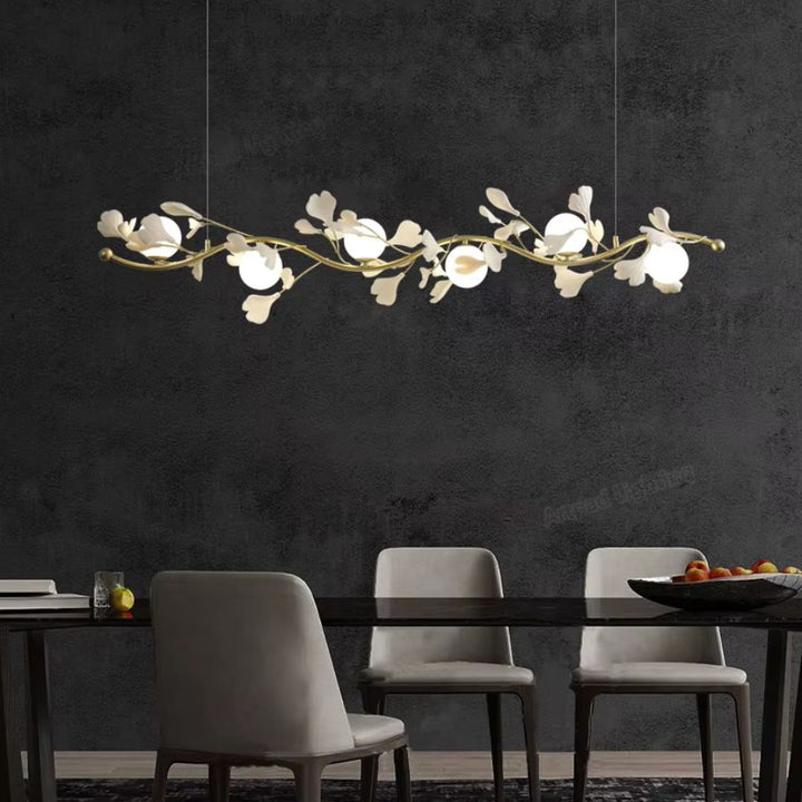 Sur fond de mur noir, suspension linéaire aux rameaux dorés, fleurs blanches et globes opalins, dans un décor moderne.