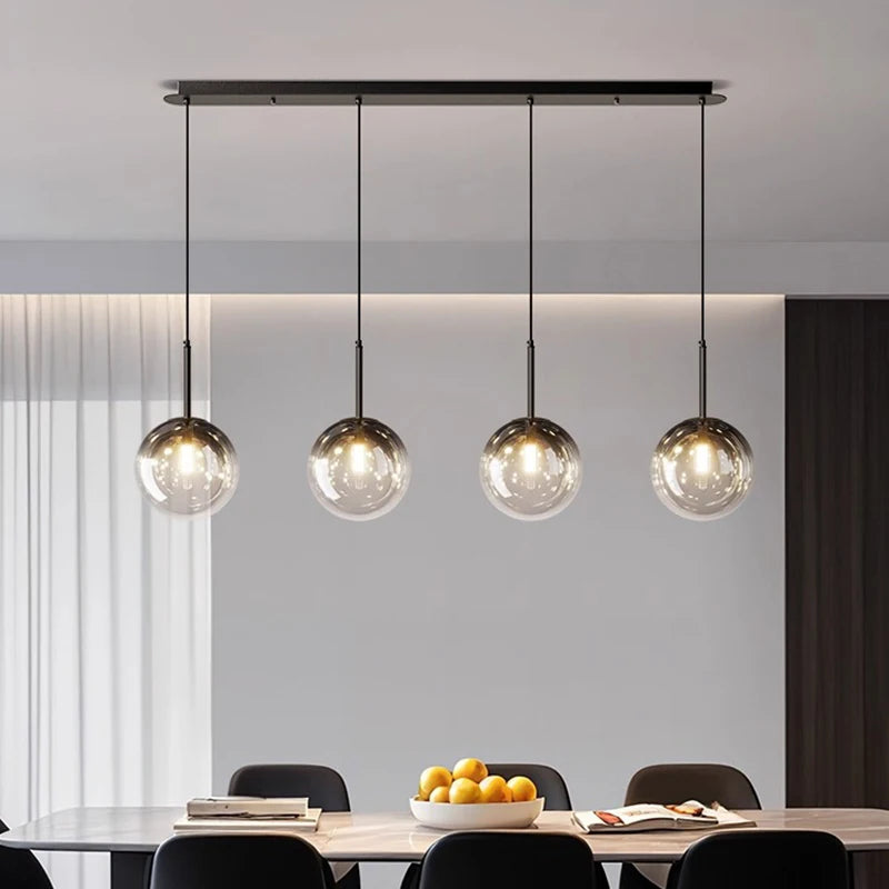 Suspension linéaire moderne à quatre globes en verre installée au-dessus d'une table de salle à manger.