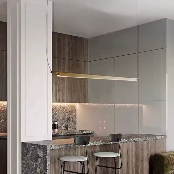 Suspension linéaire LED dorée au-dessus d’un îlot de cuisine, dans un décor contemporain aux lignes épurées