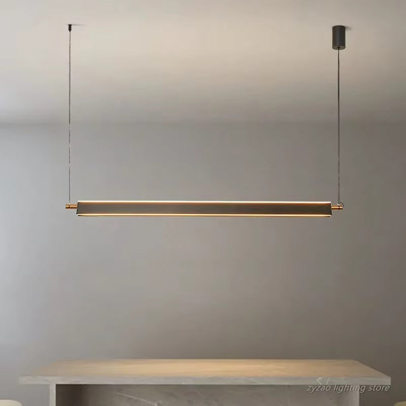 Suspension linéaire LED dorée à profil fin, installée au-dessus d’une table dans un intérieur moderne et épuré