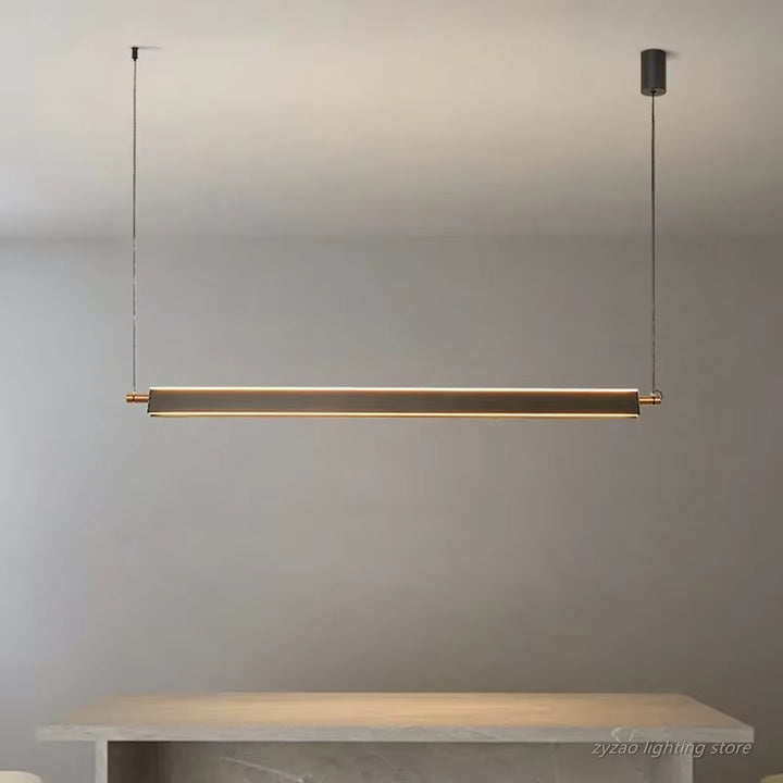 Suspension linéaire LED dorée à profil fin, installée au-dessus d’une table dans un intérieur moderne et épuré