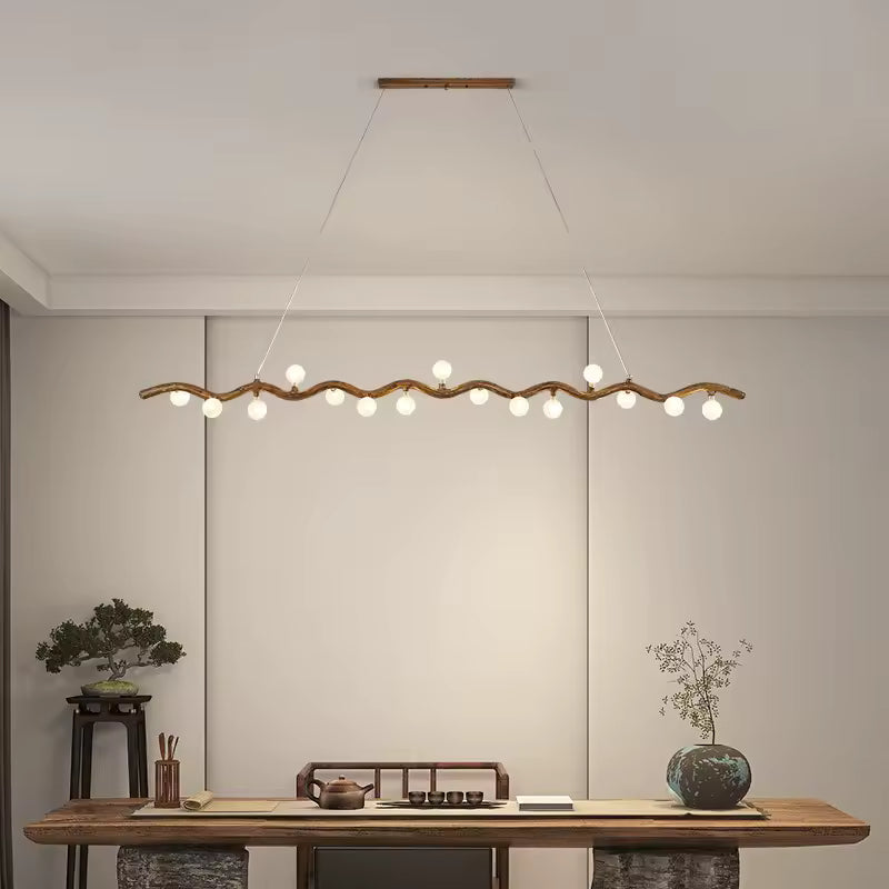 Au-dessus d'une grande table en bois, suspension linéaire à branche ondulée et globes lumineux, d'inspiration japonaise.