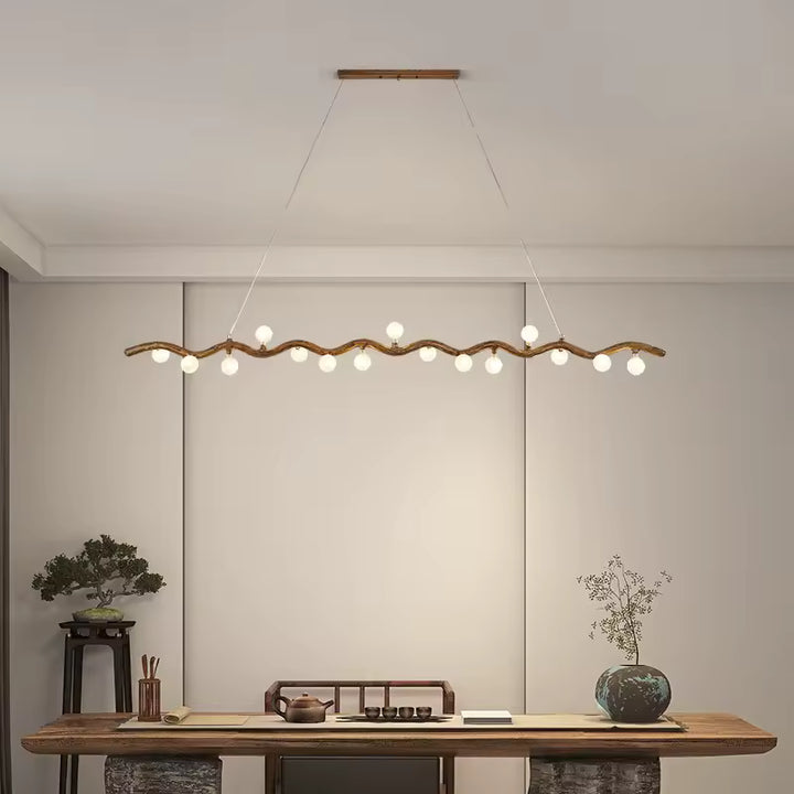 Au-dessus d'une grande table en bois, suspension linéaire à branche ondulée et globes lumineux, d'inspiration japonaise.
