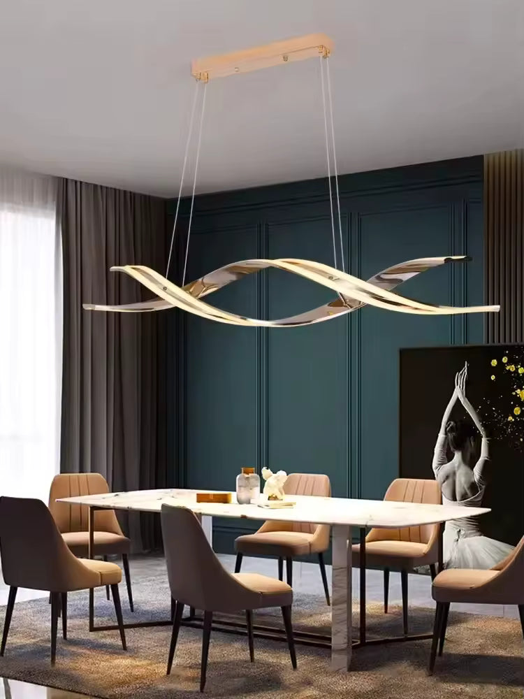 Lustre LED doré aux rubans ondulés et entrelacés, surplombant une table blanche dans une salle à manger design.