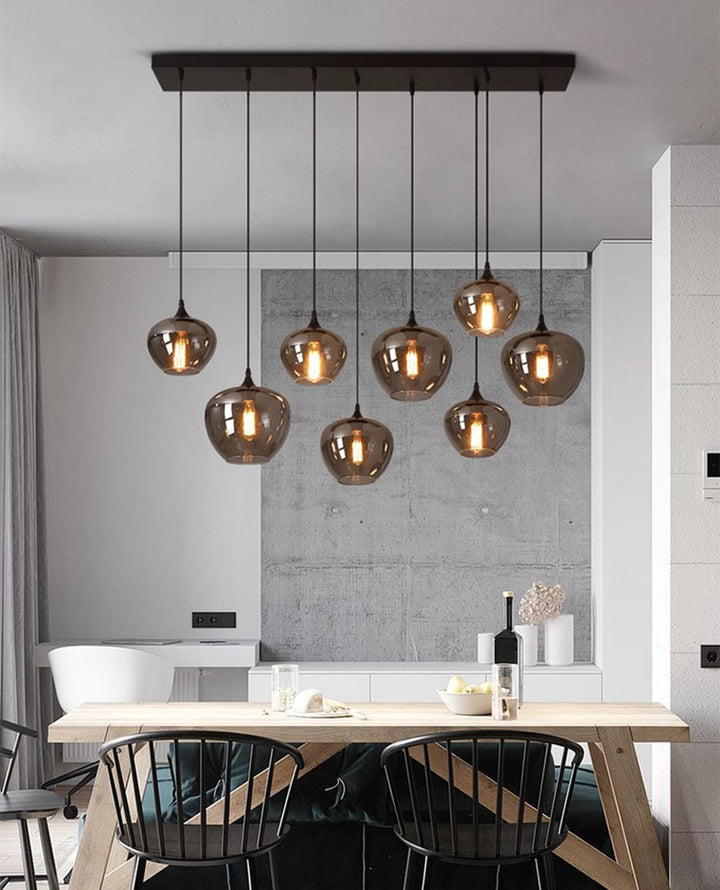 Longue suspension en verre fumé dessinant une ligne lumineuse élégante au-dessus de la table.