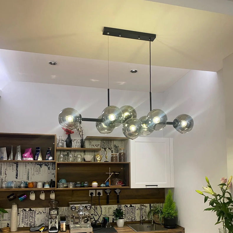 Suspension lumineuse haut de gamme en verre et métal noir installée au-dessus d'un espace bar.